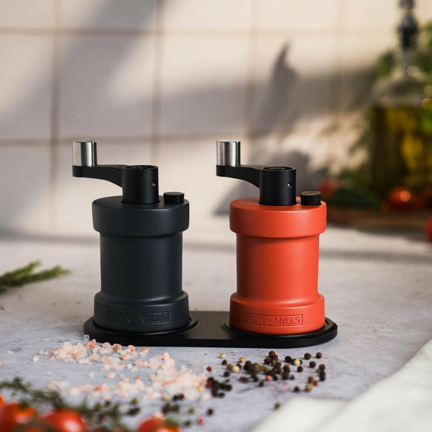 Iron-Mills anthracite grey and coral red salt and pepper mills displayed on a mill rest surrounded by seasoning