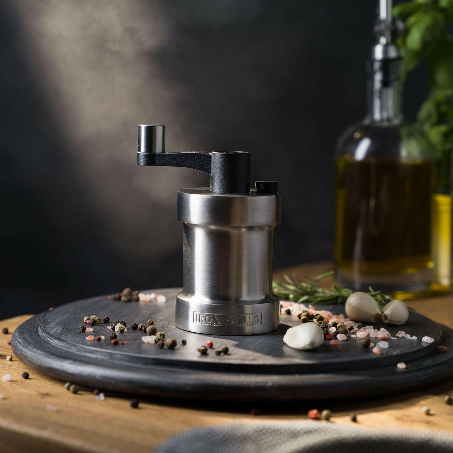 Iron-Mills brushed stainless steel salt mill on a chopping board in a premium kitchen with salt and peppercorns nearby