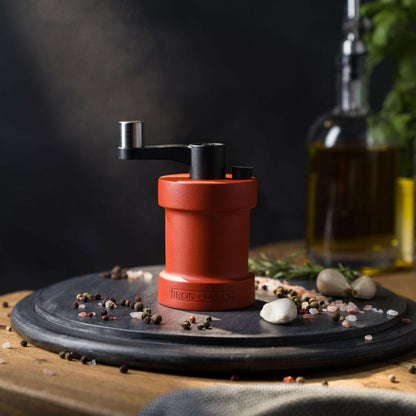Iron-Mills coral red salt mill on a chopping board in a vibrant kitchen setting with peppercorns