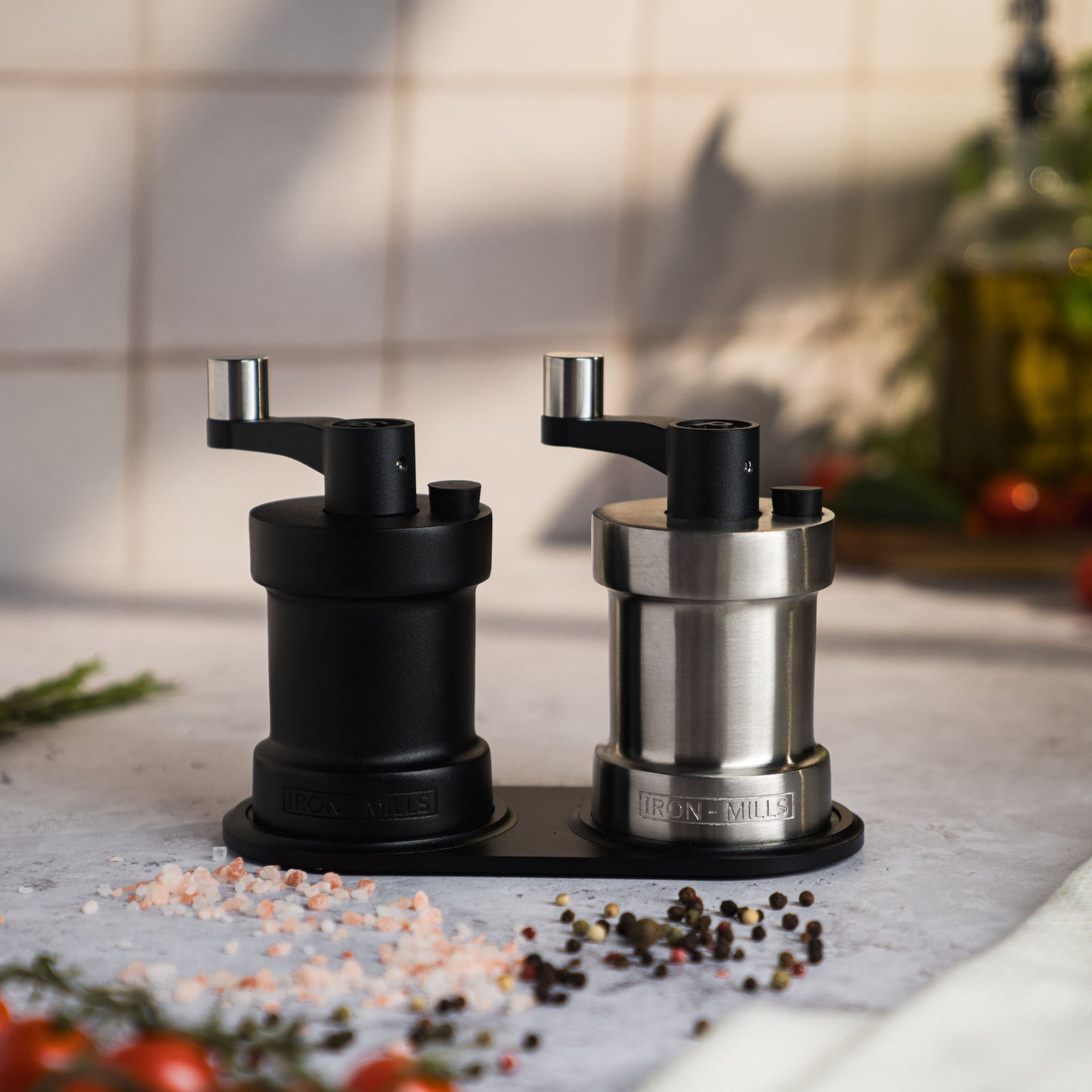 Iron-Mills onyx black and brushed stainless steel salt and pepper mills resting on a mill stand, showcasing a sleek design