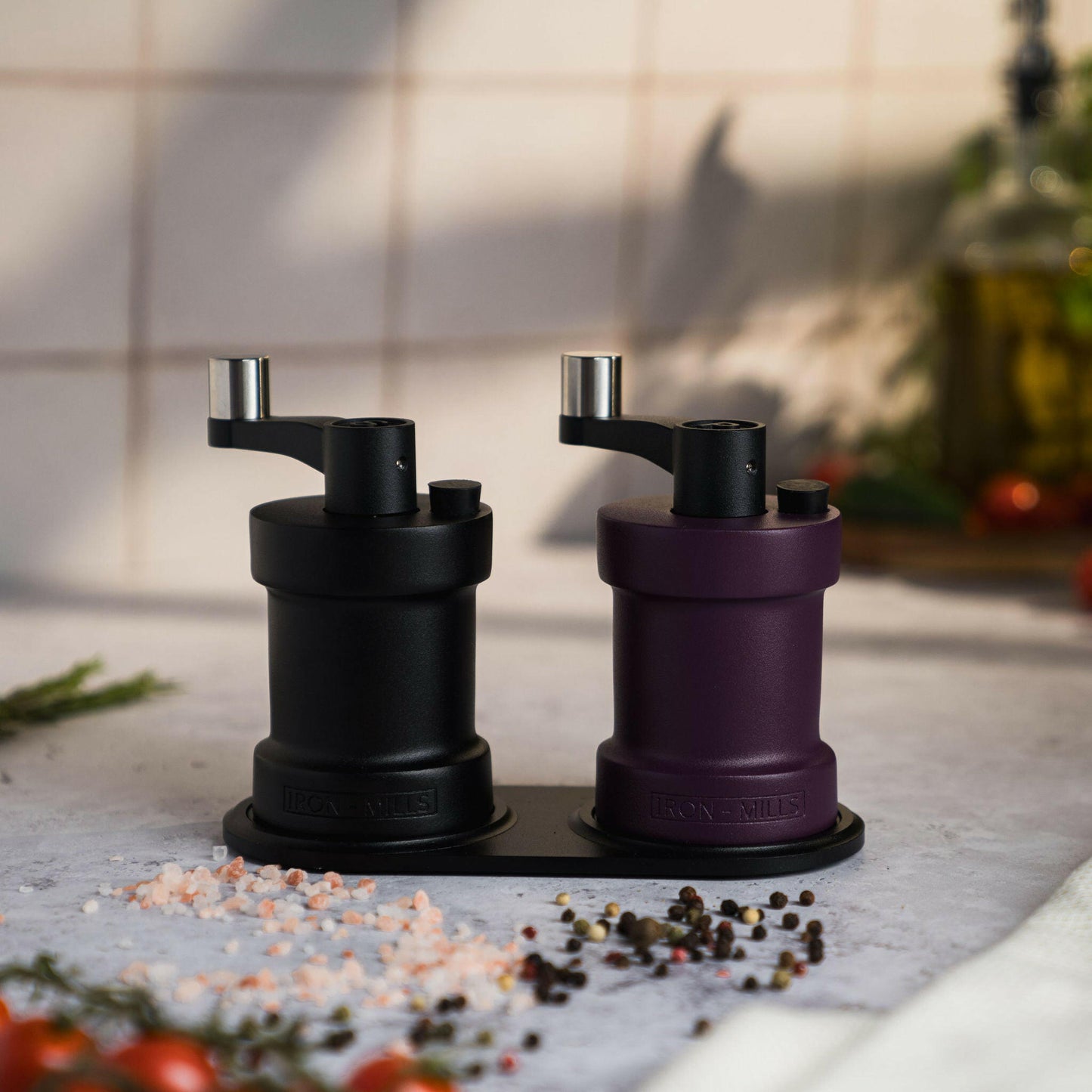 Iron-Mills onyx black and deep purple salt and pepper mills on a stylish mill rest with salt and peppercorns scattered